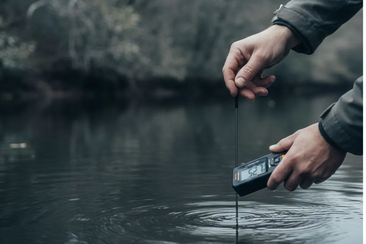 angler lowering a handheld water thermometer into a winter creek